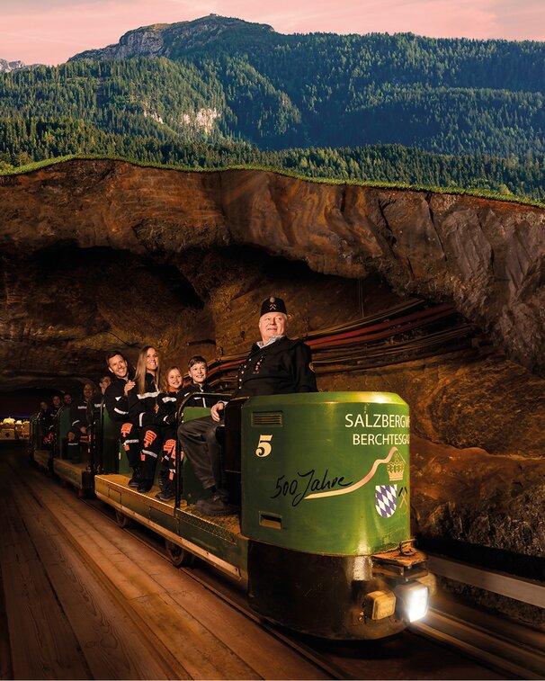 Besuchergruppe wird von einem Guide in Bergmannsuniform auf der grünen Grubenbahn aus dem inneren des Berges herausgefahren.