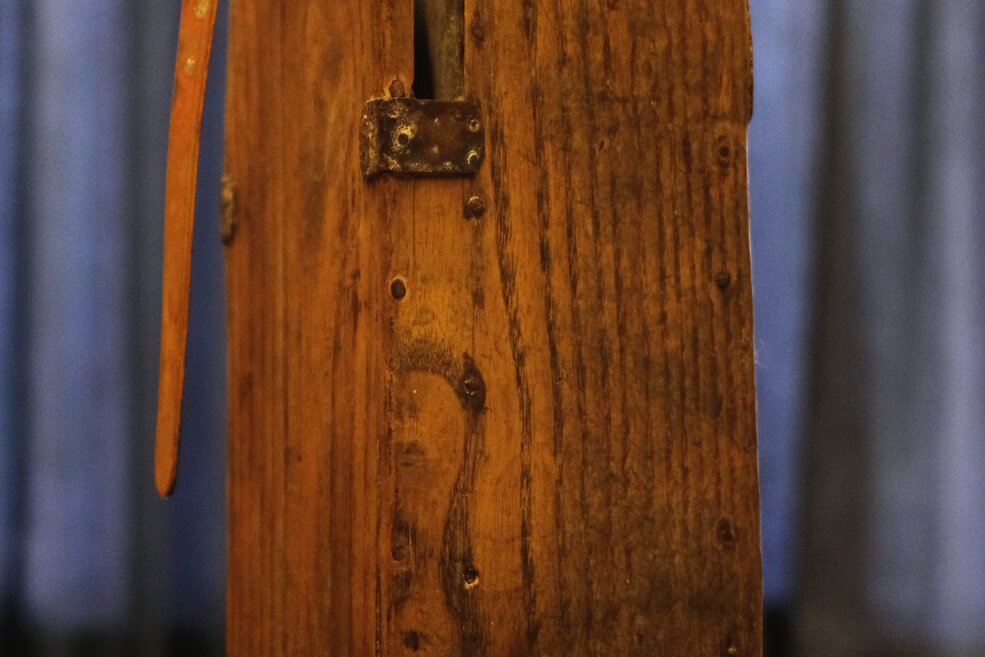 Rückseite einer kerzenbetriebenen Grubenlampe. Das verwitterte, hölzerne Gehäuse ist zu erkennen.