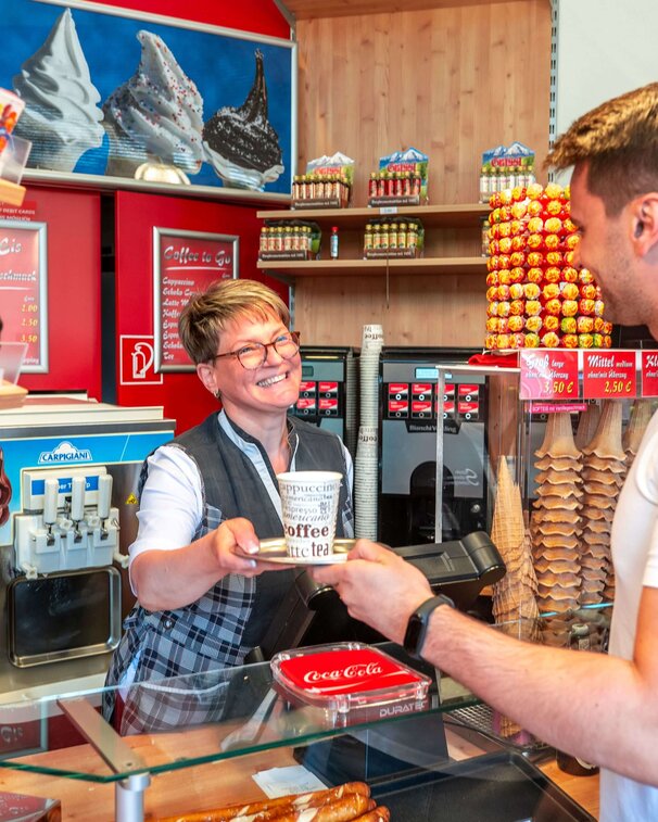 Freundliche Dame überreicht dem Herrn einen Caffee