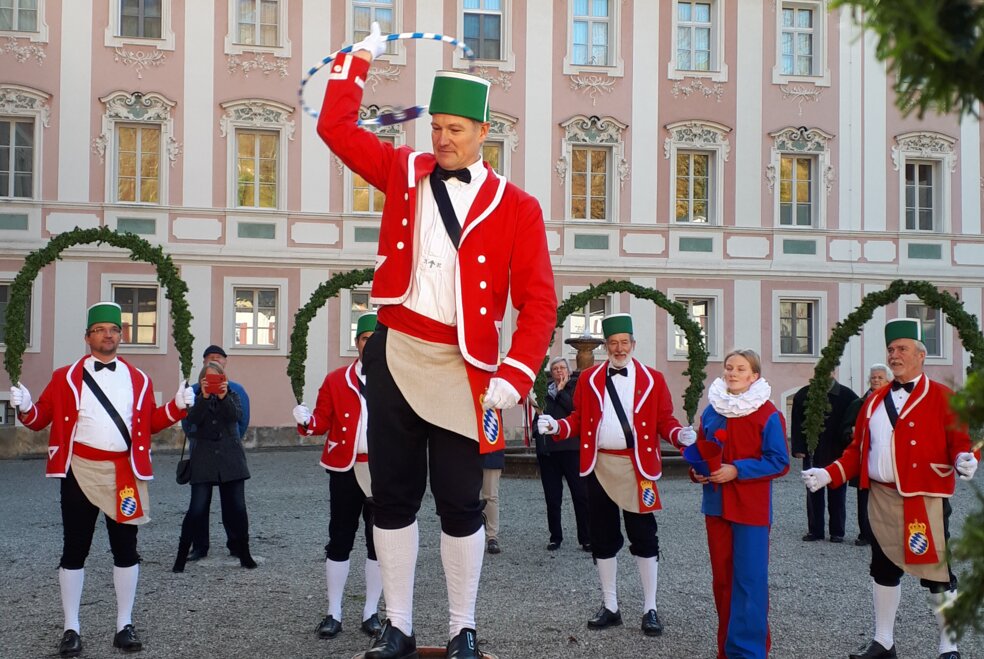 Schäffler in roter Uniform und grünem Kranz auf Holzfass stehend